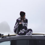 Frau mit Surfboard und wärmenden Poncho um die Schultern