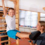 Kind und Sporttrainer trainieren zusammen an einer Sprossenwand