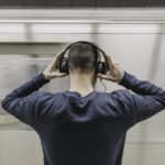 Ein Mann setzt sich Kopfhörer auf, während eine U-Bahn vorbei fährt.