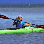 Frau fährt Kajak mit Schwimmweste und Sonnenschutz