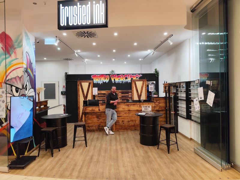 Eingangsbereich eines Tattoo- und Piercingstudios mit Empfangstresen und einem freundlichen Tätowierer.