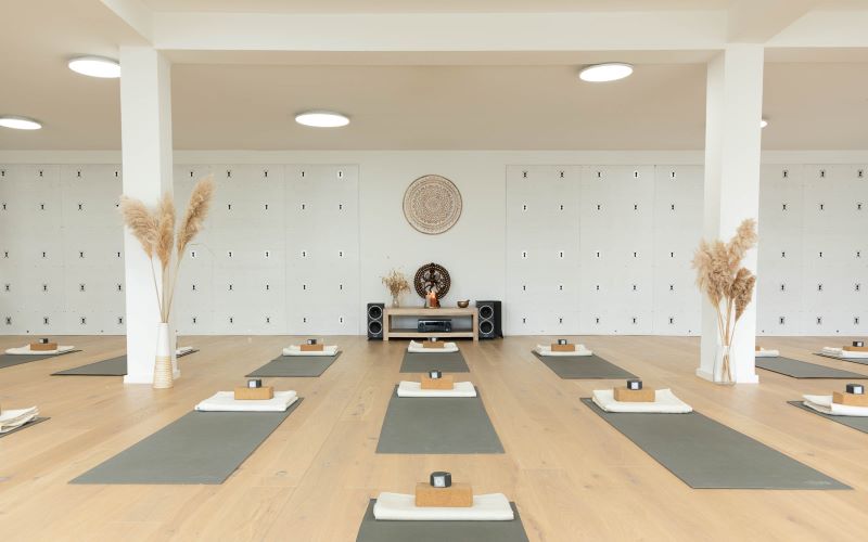 Ein heller, minimalistischer Yoga-Raum, vorbereitet mit Matten, Blöcken und Handtüchern.