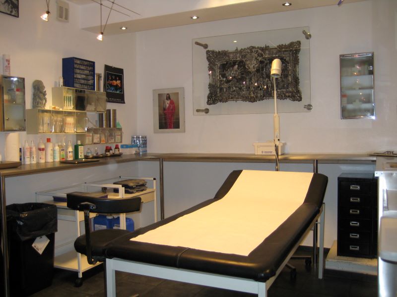 Behandlungsraum in einem Tattoo-Studio, ausgestattet mit einem Behandlungstisch und Regalen für Tattoozubehör.