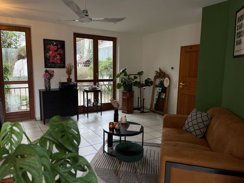 Gemütliche, wohnliche Studio-Atmosphäre mit Pflanzen, Sofas und dekorativen Elementen, die eine entspannte Umgebung für Tattoo-Sitzungen schaffen.