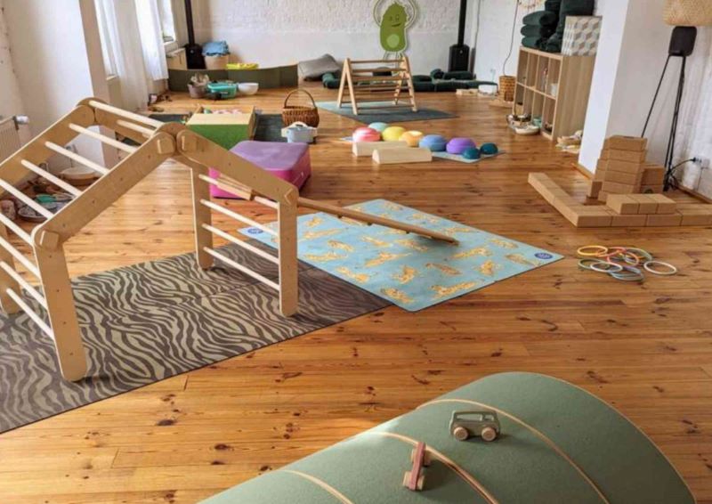 Ein heller Raum mit Holzboden, gefüllt mit Spielgeräten und Yoga-Ausrüstung, die auf Kinder abgestimmt sind.