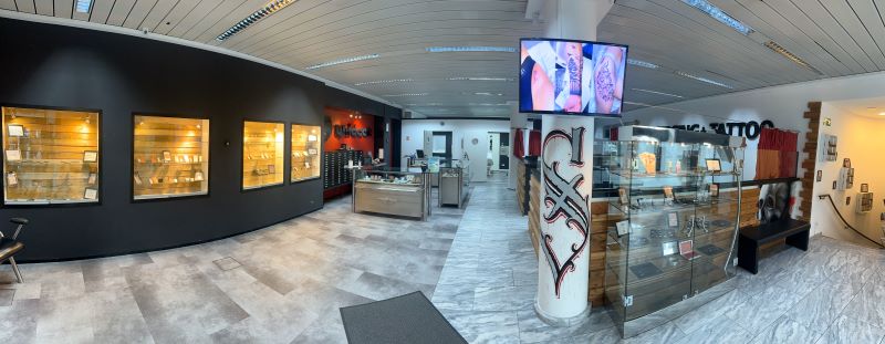 Panoramablick auf das Tattoo- und Piercing-Studio mit modernen Vitrinen und einer professionellen Empfangstheke, die eine entspannte Atmosphäre vermitteln.