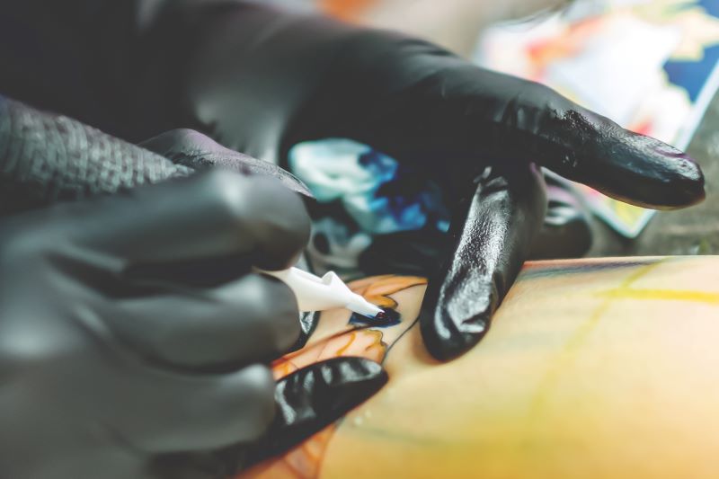 Tattoo-Künstler arbeitet an einem farbigen Tattoo auf der Haut eines Kunden.