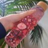 Hand hält eine mit floralen Mustern bedruckte Waterdrop-Flasche vor einer Pflanze.