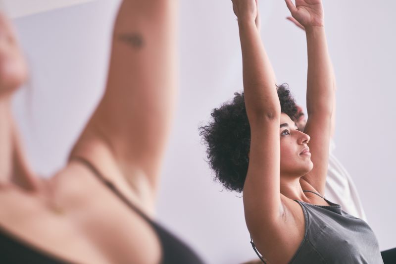 Nahaufnahme von Teilnehmern in einer Yoga-Stunde, die ihre Arme in die Luft strecken.