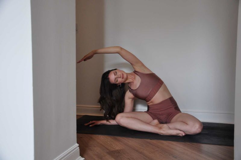 Eine Frau in einer seitlichen Dehnungs-Yogapose auf einer Yogamatte in einem Innenraum.